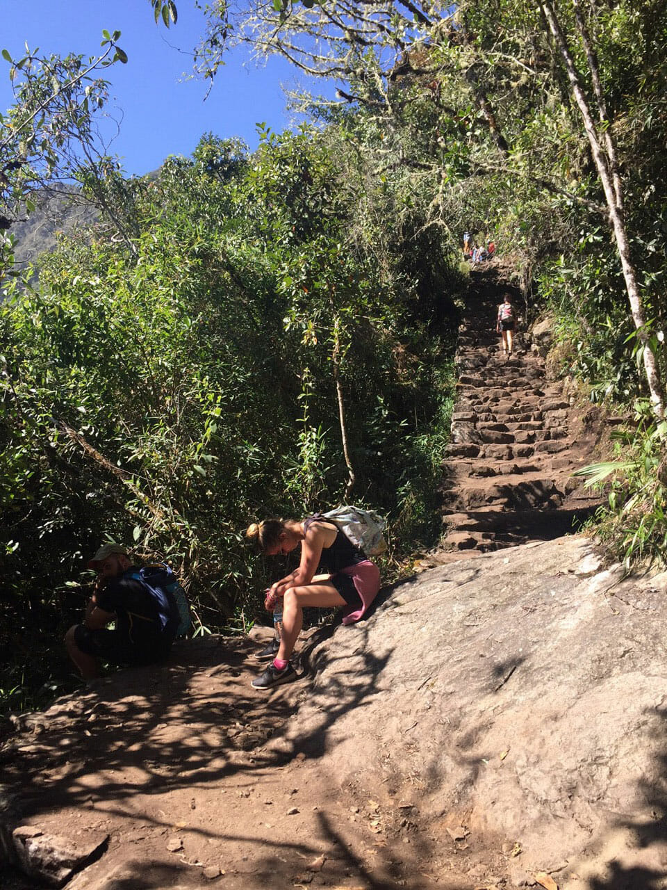 Una mujer se sienta con la cabeza gacha descansando cerca de los escalones del sendero de la montaña Machu Picchu