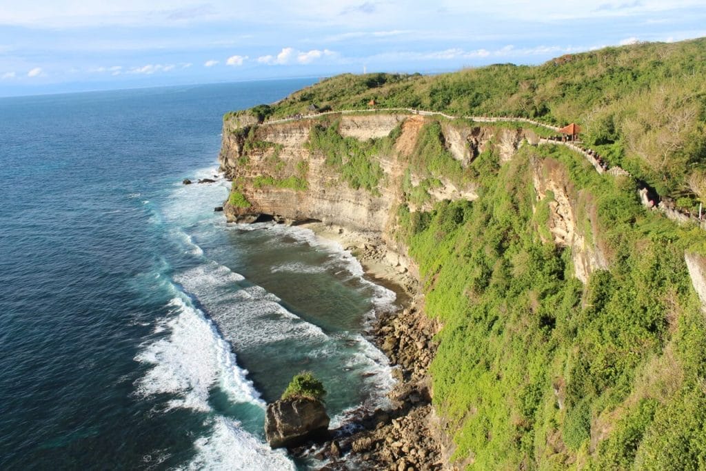 Un acantilado en la costa suroeste de Bali cubierto de maleza y una playa de aguas cristalinas