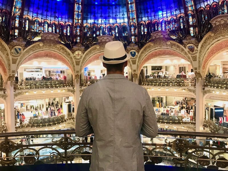 A man wearing a grey blazer and a white hat standing looking at tehe famous Galeries Lafayette glass cupola, Paris, France