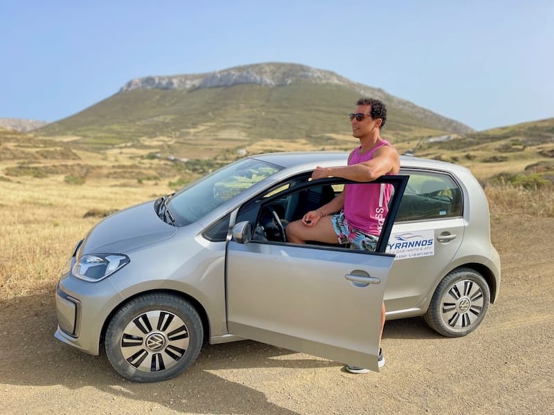 Pericles Rosa posing for a picture with an eletric car and a mountain in the backdrop in Astypalea, Greece