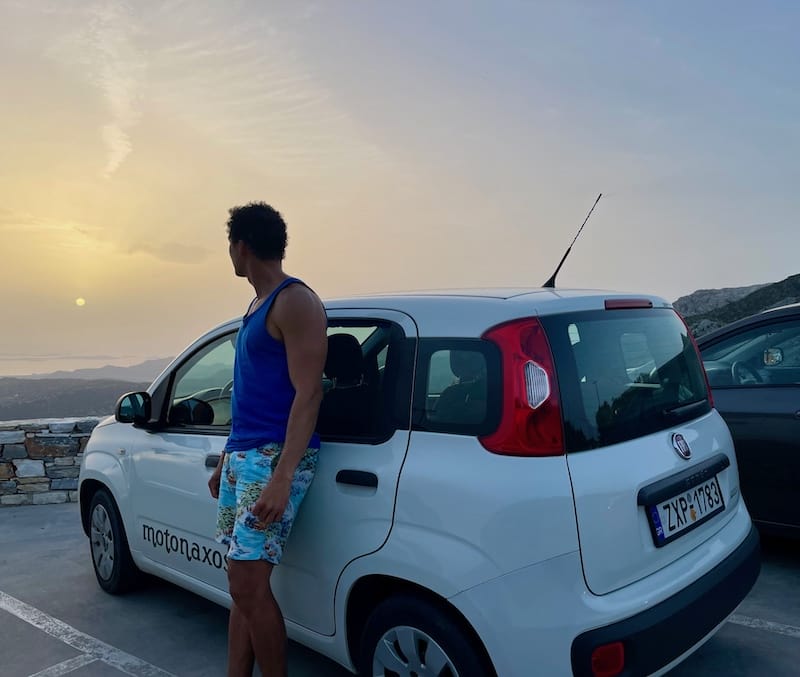 um homem encostado num Fiat Panda observando o pôr do sol, Naxos, Grécia